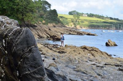 Rear view of man on rock by river against sky