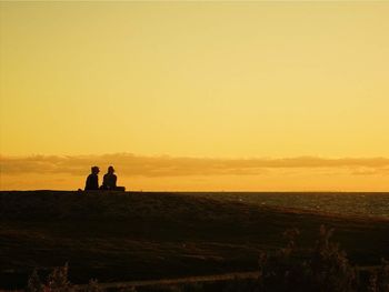 Silhouette people on landscape against clear sky during sunset