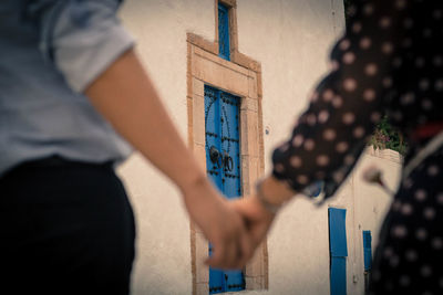 Midsection of couple holding hands while standing against building