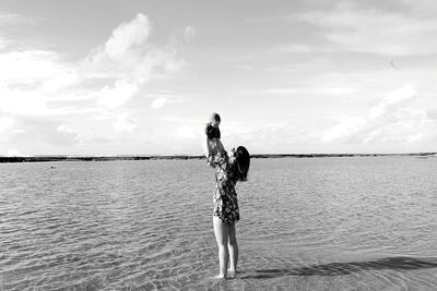 Rear view of woman standing at beach against sky