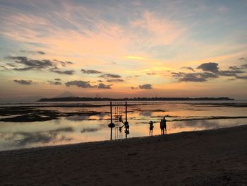 Silhouette people at beach against sky during sunset