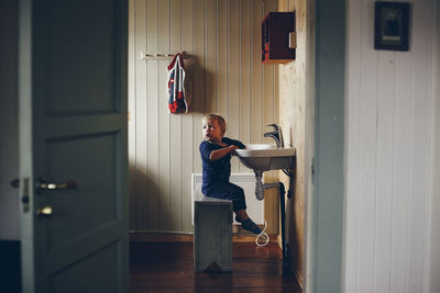 Side view of boy sitting by sink at home