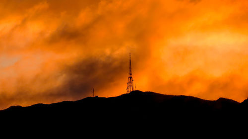 Low angle view of silhouette communications tower against sky during sunset