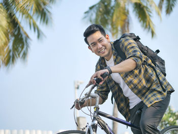 Smiling man sitting on bicycle against palm trees