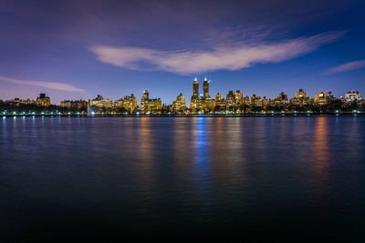 Scenic view of river by illuminated buildings against sky
