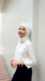 Young woman looking away while standing against white wall