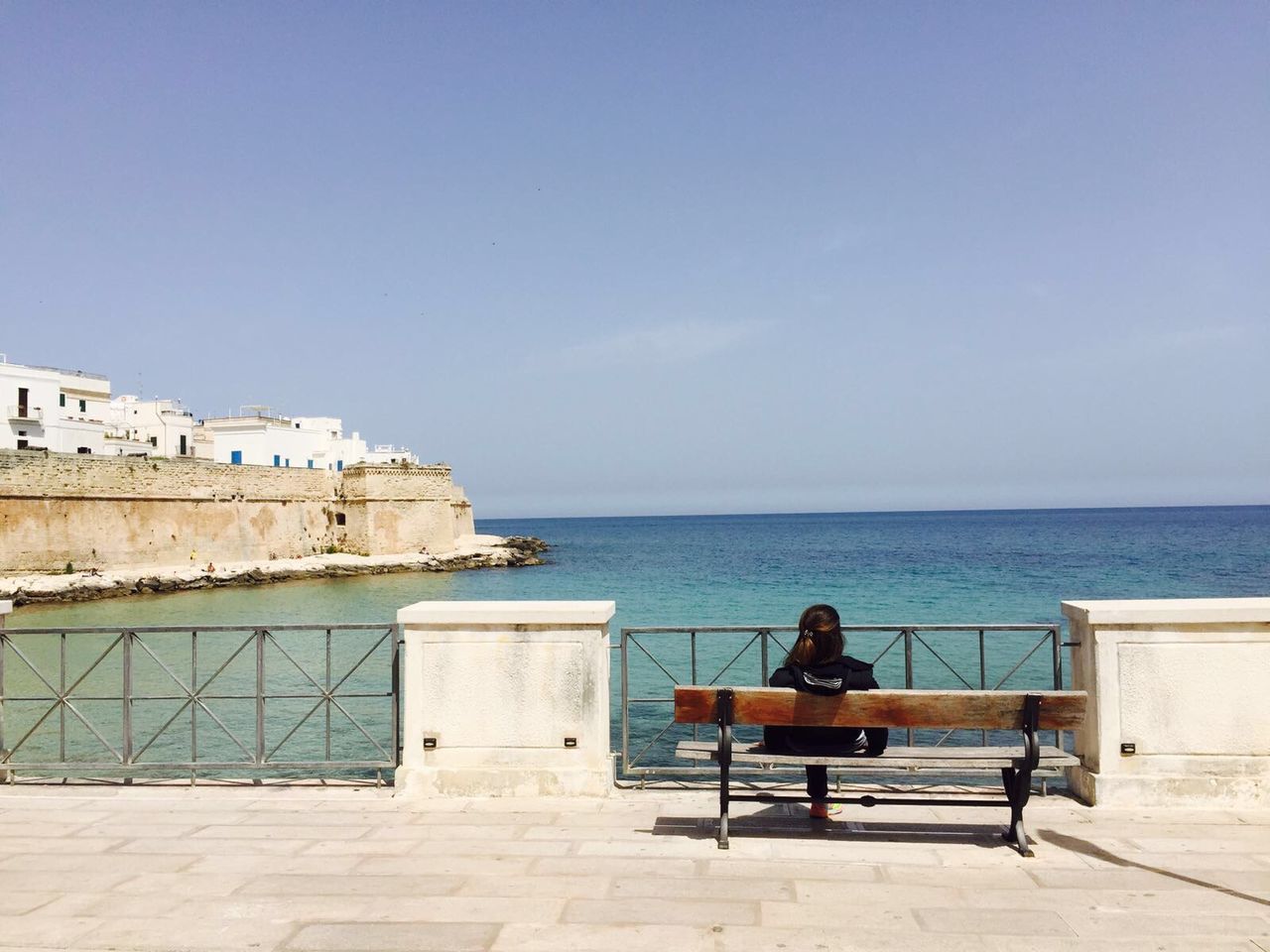 sea, water, sitting, lifestyles, horizon over water, leisure activity, men, built structure, architecture, copy space, person, clear sky, relaxation, rear view, building exterior, sky, bench, railing