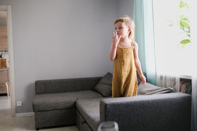 Child jumps and plays on sofa in minimalist living room, gray sofa.