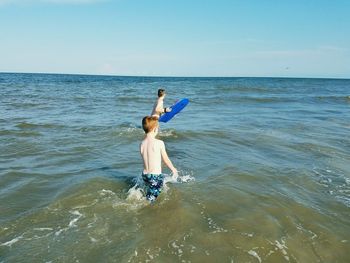 Boys playing in sea against sky on sunny day