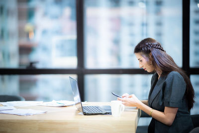 Side view of woman using mobile phone at table