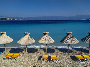 Deck chairs and parasols on beach against blue sky