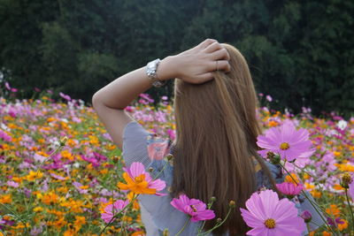 Rear view of woman with hand in head while standing by flowering plants