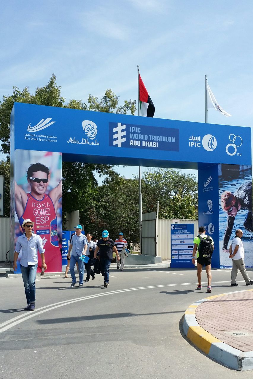 text, western script, men, communication, information sign, sign, street, non-western script, road sign, person, large group of people, road, walking, guidance, lifestyles, transportation, information, sky, flag