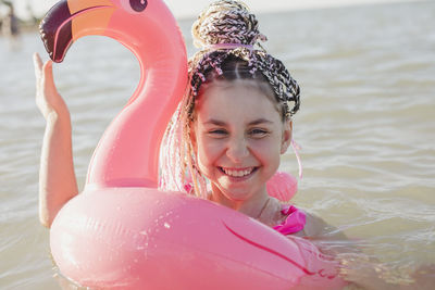 Happy girl with braided hair enjoying in pink flamingo inflatable ring