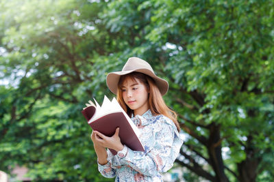 Portrait of woman wearing hat standing against trees