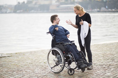 Disabled man on wheelchair taking with female caretaker by lake