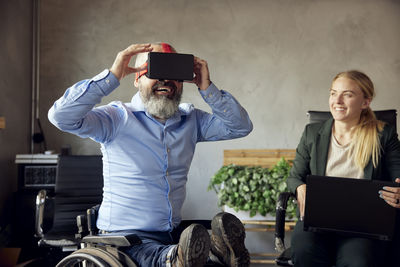 Blond businesswoman looking at businessman wearing vr simulator in creative office