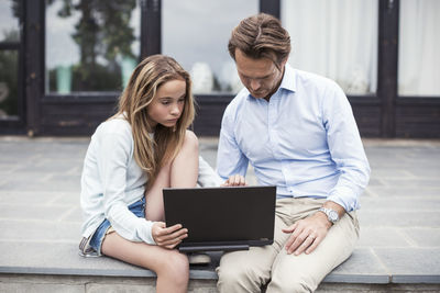 Father and daughter using laptop together at porch