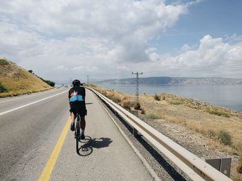 Rear view of man riding bicycle on road against sky