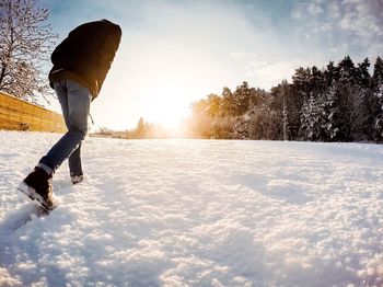 Man walking on snow covered field against sky