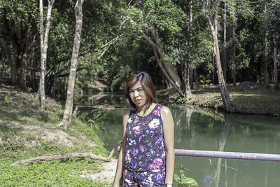 Portrait of beautiful woman standing with stream and trees in background