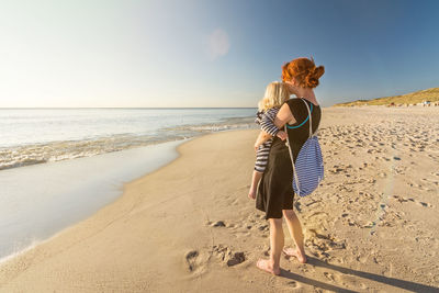 Rear view of woman on beach against sky