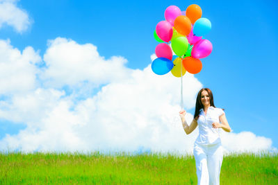 Woman holding colorful balloons on field against sky