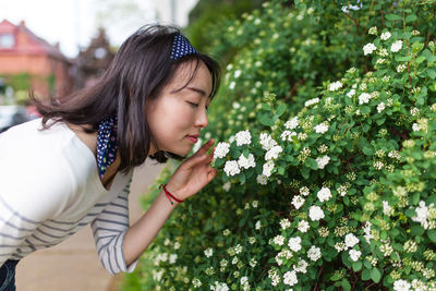 Side view of woman smelling flower blooming on plant at park