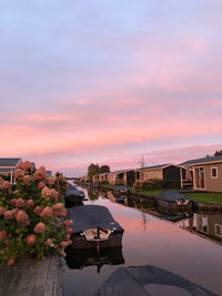 Houses by canal against sky during sunset