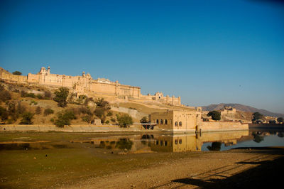 Historic building by lake against clear blue sky