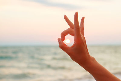 Close-up of hand against sea during sunset