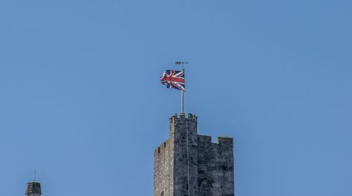 Low angle view of flag by building against clear blue sky
