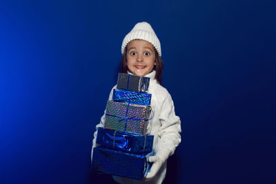 Christmas boy child in a white knitted sweater and hat stands in the studio against gifts boxes