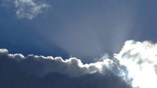 Low angle view of sunlight streaming through clouds