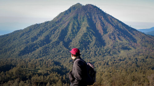 Side view of young man looking at mountain against sky