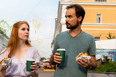 Young couple talking while walking along city street and eating takeaway food