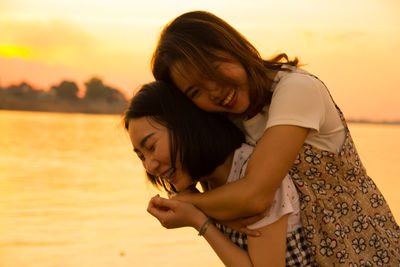 Woman piggybacking friend against sky during sunset