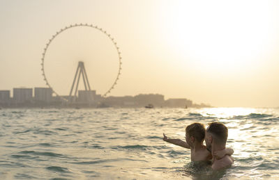 Rear view of woman in sea against sky during sunset