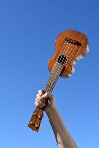 Low angle view of person holding guitar against clear blue sky