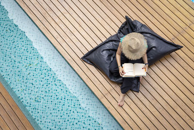 High angle view of woman reading book while sitting by swimming pool
