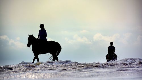 People riding horses at beach against sky