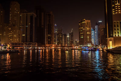 River by illuminated buildings against sky at night