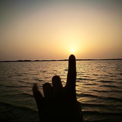 Silhouette hand against sea during sunset