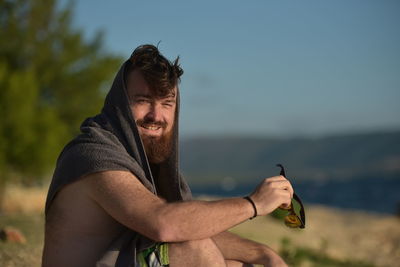 Portrait of bearded man sitting at beach against sky