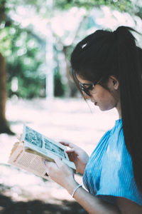 Side view of young woman reading book outdoors