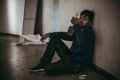 Young man smoking cigarette while sitting on floor at home