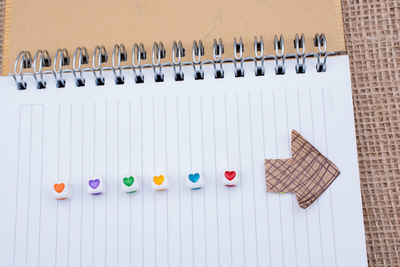 Close-up of multi colored heart shapes with arrow symbol on spiral notepad