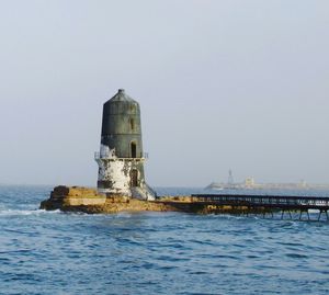 Lighthouse by sea against clear sky