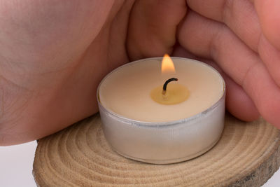 Close-up of hand covering tealight candle on wood