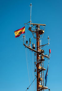 Low angle view of spanish flag on mast against clear blue sky